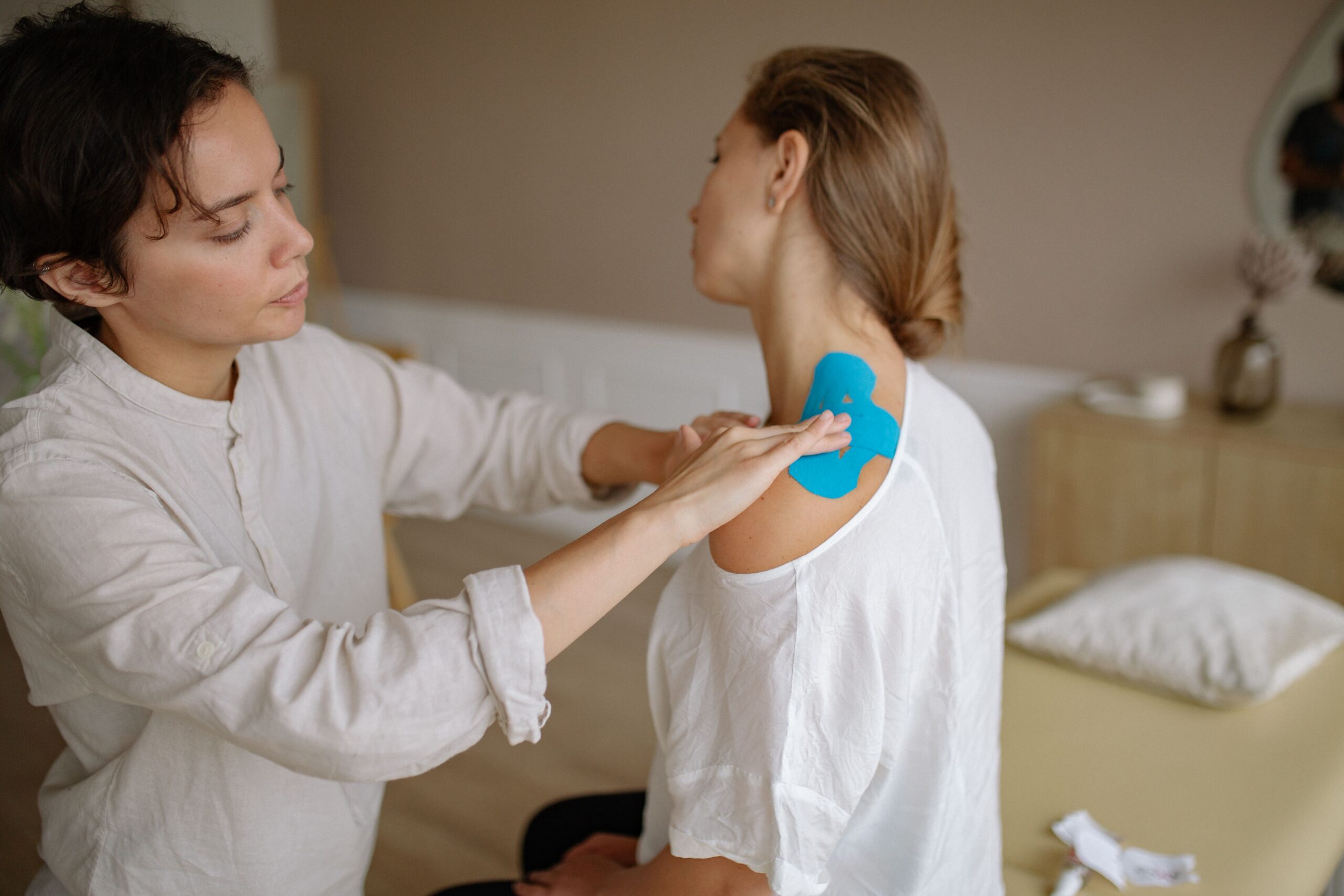 Ein Massagetherapeut bringt während einer Rehabilitations- und Sporttherapie-Sitzung Kinesiologie-Tape am oberen Rücken eines Klienten an.